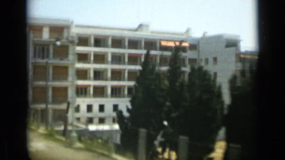 1962 Monaco home-movie frame showing a white residential block with balconies, shutters, and trees in front.