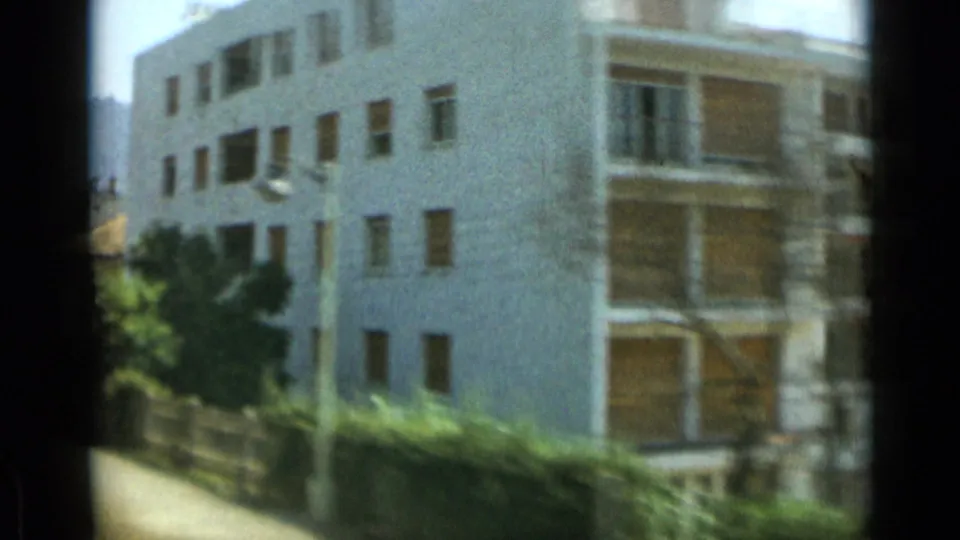 1962 Monaco frame of a white apartment facade with shuttered openings, balconies, trees, and a low boundary wall.