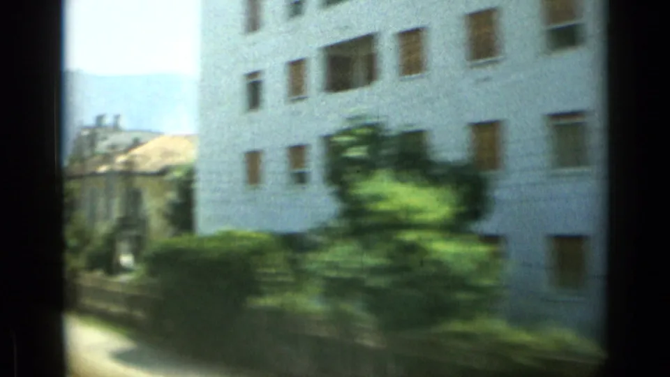 1962 Monaco train-window view passing a white apartment block and greenery, with soft focus and 8mm motion blur.