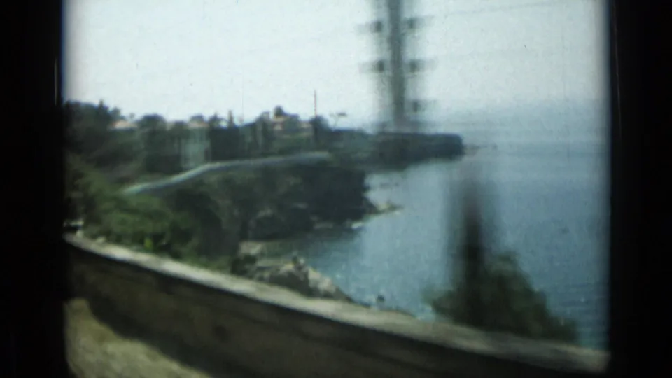 Moving 8mm view from a Monaco train over the coastal waterline, with shoreline walls, vegetation, and heavy motion blur.