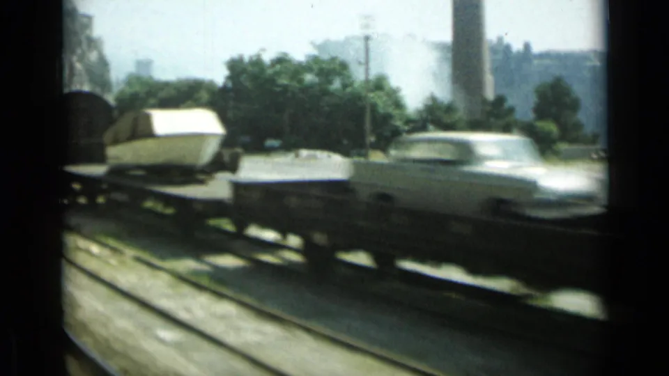 A white mid-century sedan on a rail flatcar passes close to the camera in the 1962 Monaco footage.