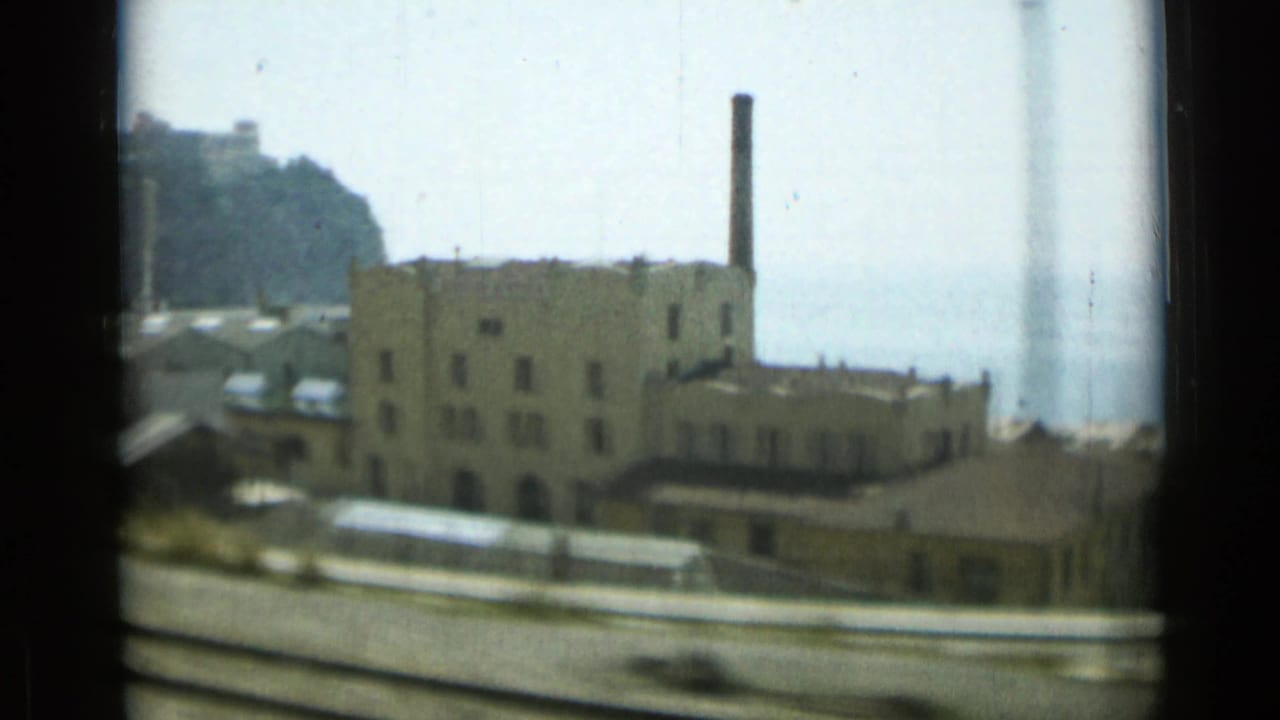 Industrial building with chimney beside water, seen from a moving vehicle.