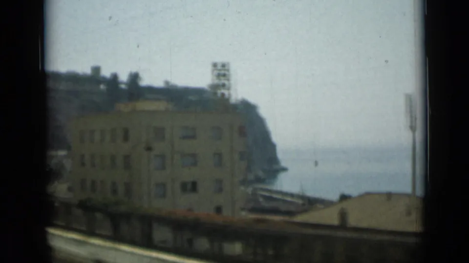 Final Monaco frame shows the passing building, hillside structures, coastal water, and blurred foreground rail or road edge.