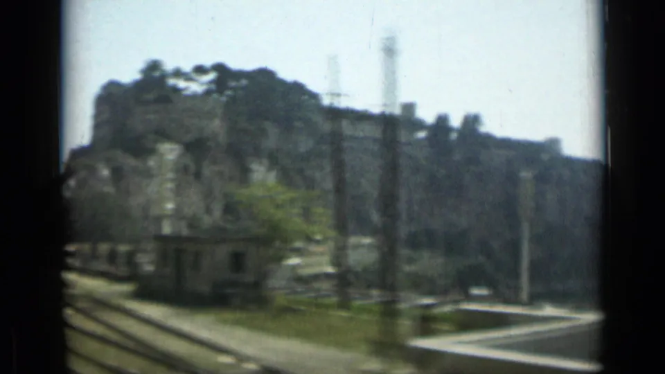 1962 Monaco roadside frame showing a rocky cliff, utility poles, a small structure, and a curving coastal road.