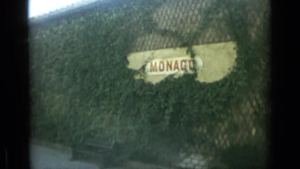 Close view of a weathered MONACO sign partly covered by ivy, filmed in soft 8mm color at the end of the clip.