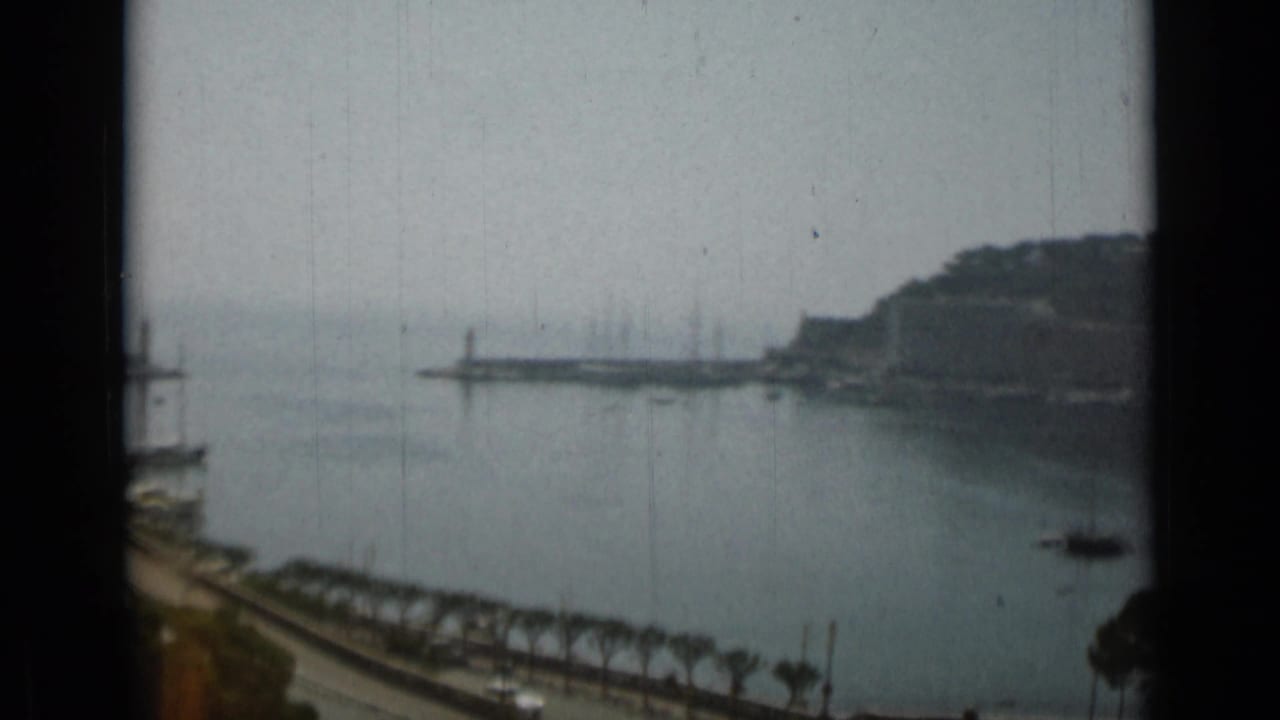 Harbor entrance with breakwaters, calm water, hillside shoreline, and a small boat.