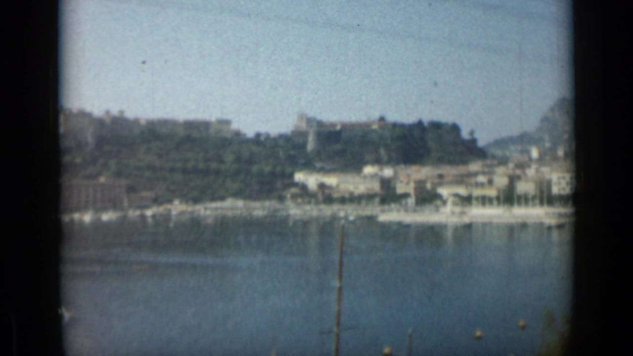 Harbor water seen through a dark window frame with shoreline buildings and trees beyond.