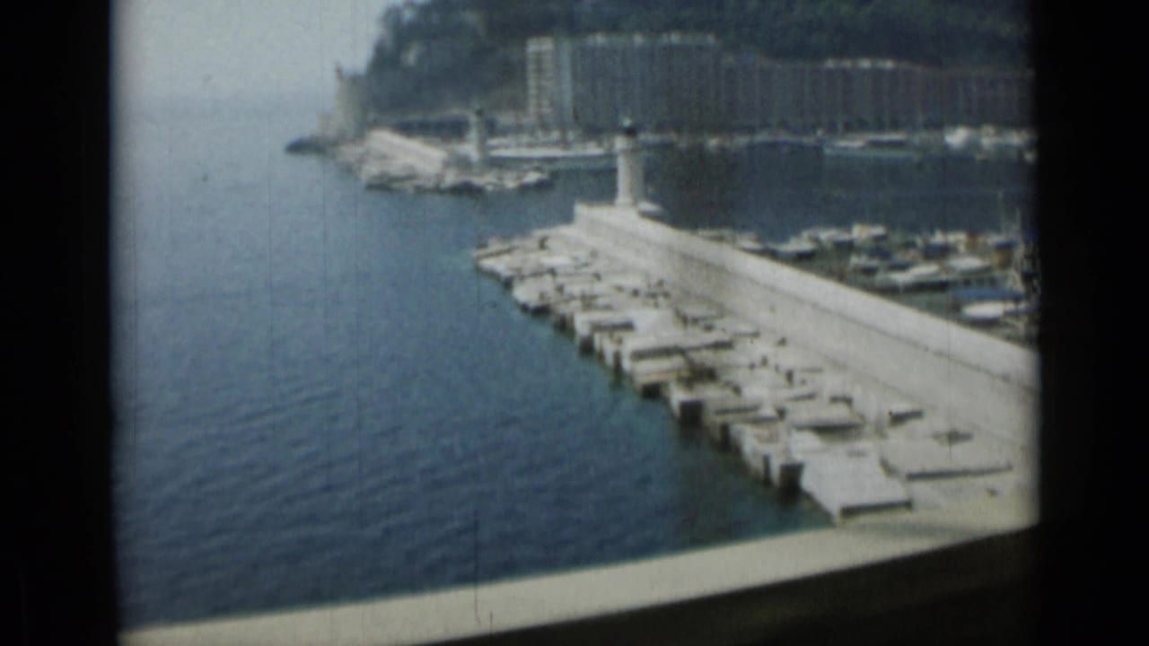 Concrete marina pier with boats and hillside buildings across the water.