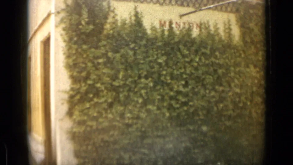 1962 travel footage passes a dense hedge and wall where the place name Menton is visible in red lettering.