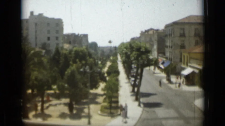 1962 Monaco home-movie frame looking down a broad palm-lined street with awnings, pedestrians, and mid-century urban facades.