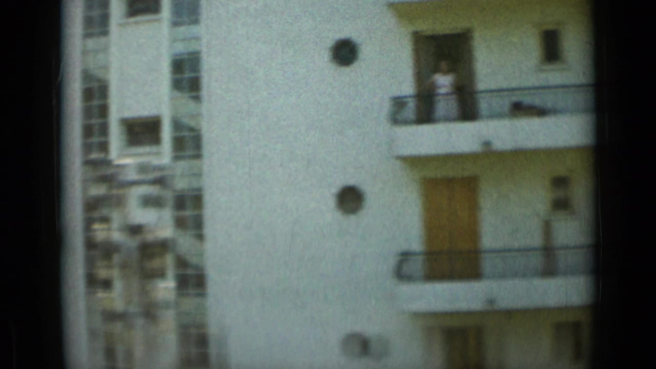 Monaco apartment facade with balconies and a visible person standing on an upper balcony in 1960s home-movie footage.