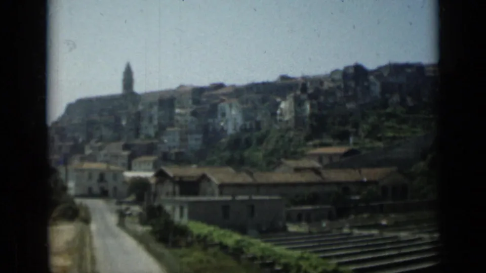 Soft 8mm Monaco hillside view with clustered buildings, a tower, rooftops, roadways, and foreground rail-like lines.