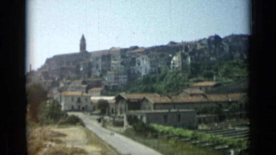 Wide 1962 Monaco cityscape with a hillside skyline, tower, road, trees, rooftops, and foreground track-like lines.