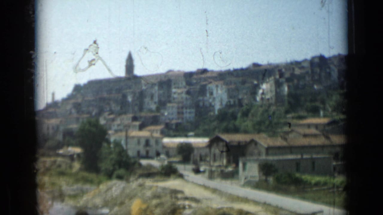 Hillside buildings and church steeple seen beyond a road and trees.