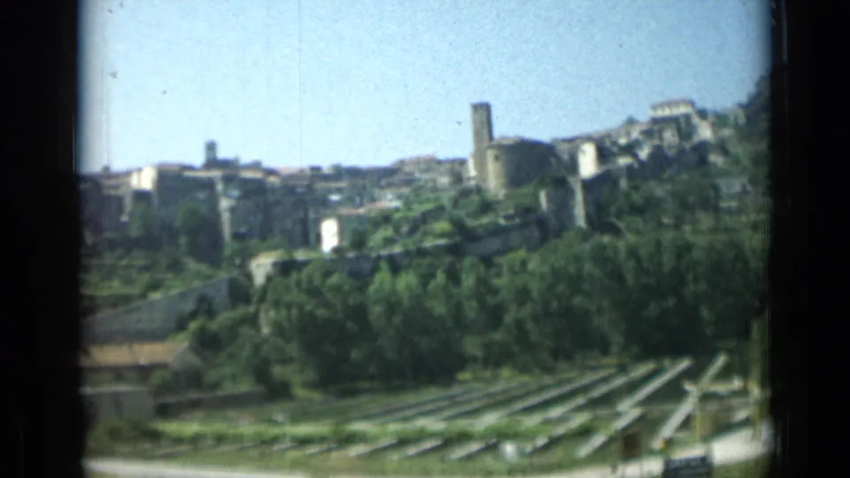 1962 Monaco frame showing a stone tower, hillside buildings, dense trees, and rows of cultivated or terraced greenery.