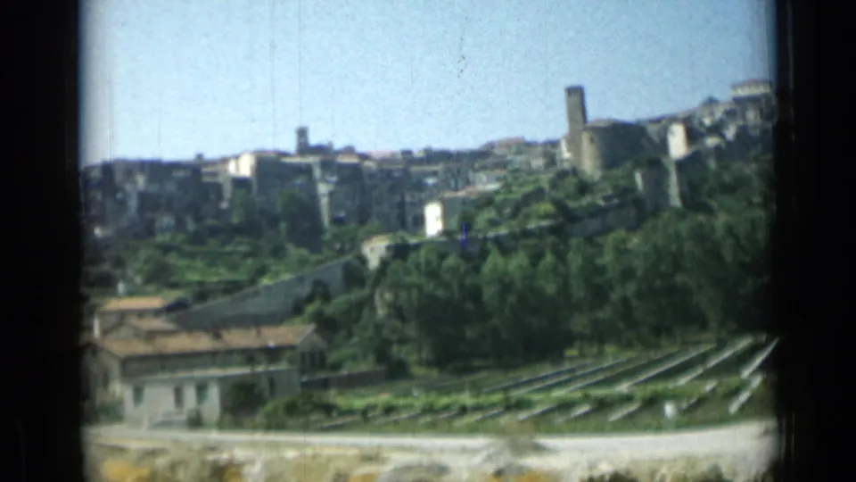 1962 Monaco home-movie frame with hillside buildings, a tower, roadside foreground, trees, and terraced or cultivated rows.