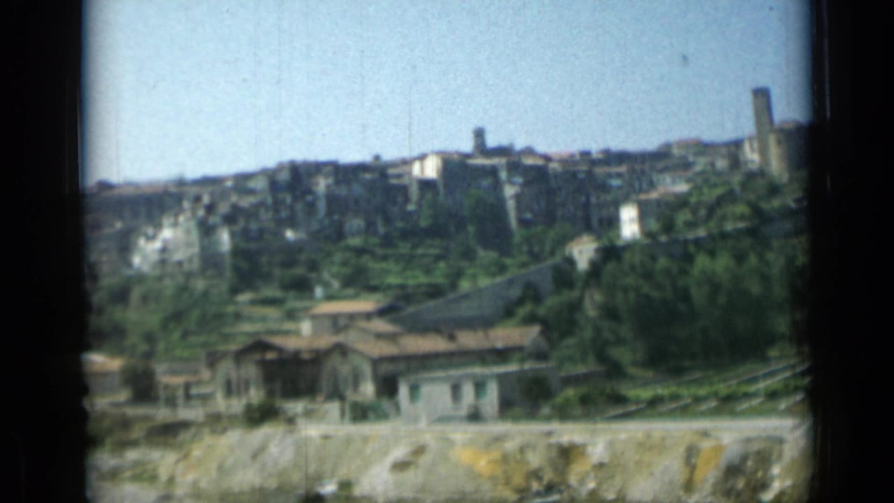 Similar hillside view with clustered buildings, terraces, low houses, and transport lines below.
