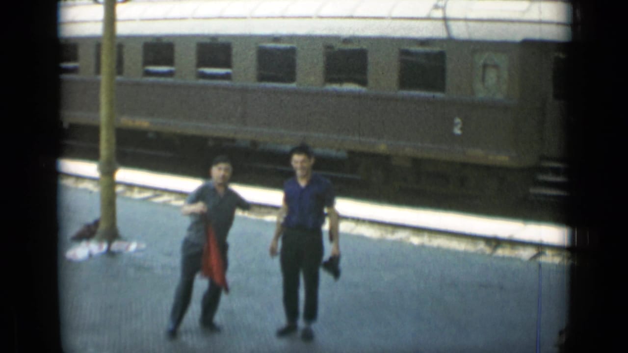 Two men walk on a station platform beside a dark passenger train car.