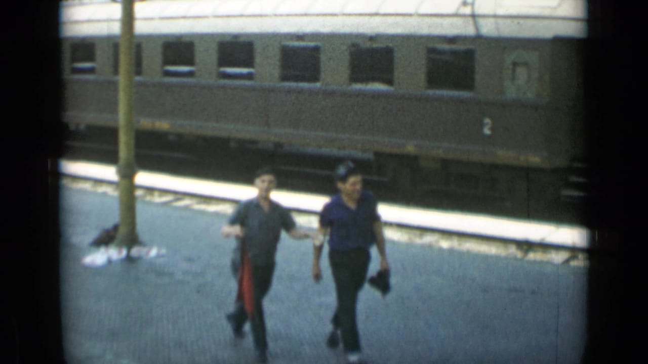 Two men continue walking past a pole with the train car behind them.