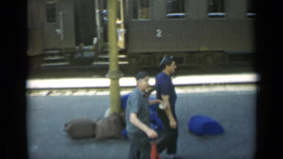 At the end of the Monaco station shot, the men move out of frame while bags or bundles sit near the stopped passenger train.
