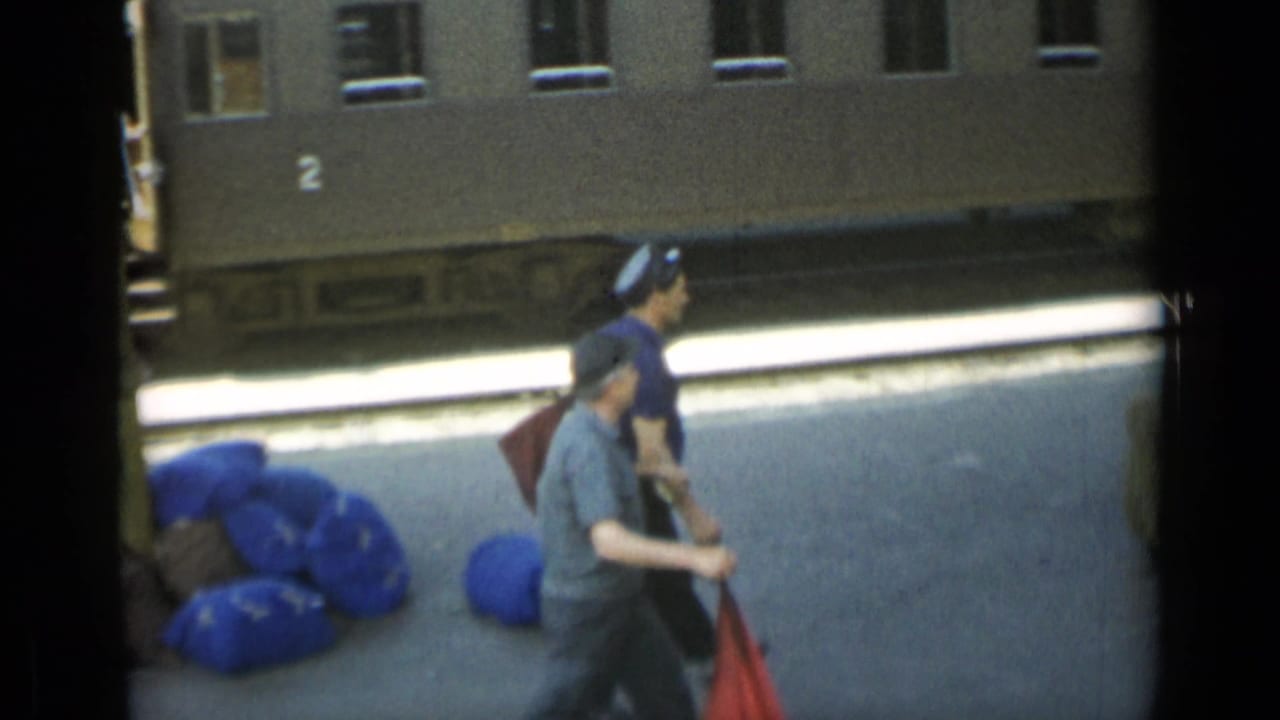 Uniformed men and travel bags on a train platform beside a stationary rail carriage.