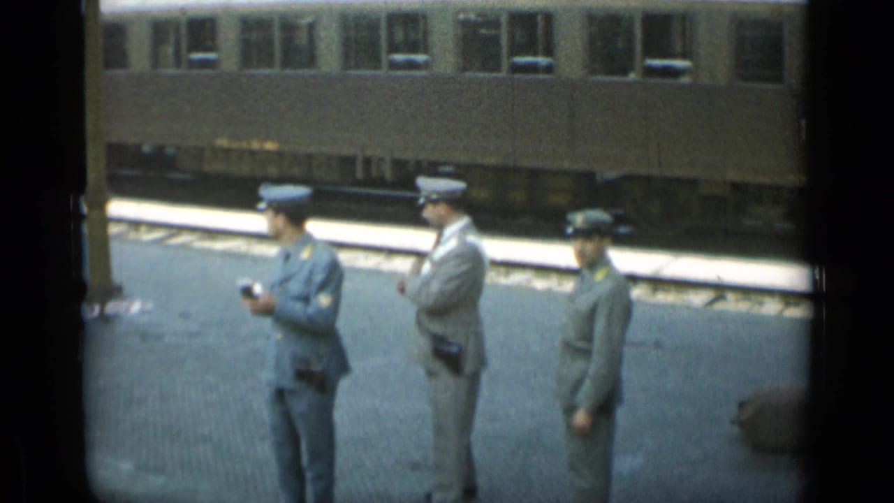Three uniformed men stand on a platform in front of a stopped passenger train.