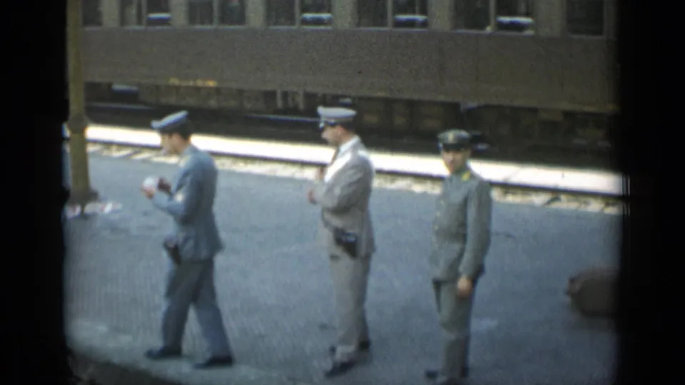 A 1962 Monaco platform view shows three uniformed station officers, one moving across frame, with the train carriage behind them.