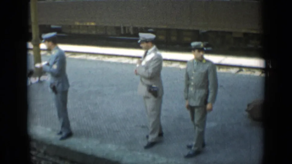 The closing 1962 Monaco frame shows three uniformed station officers spaced across the platform beside a stationary passenger train.