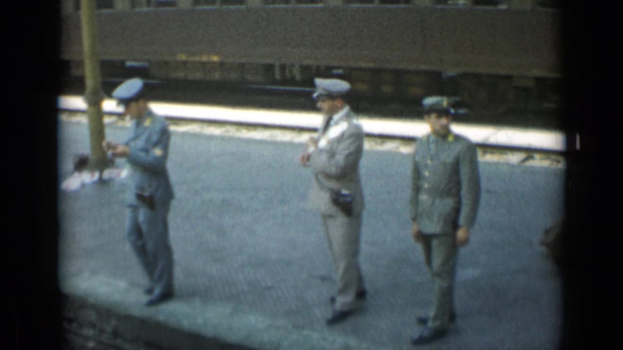 Three uniformed men stand on a rail platform beside train tracks.