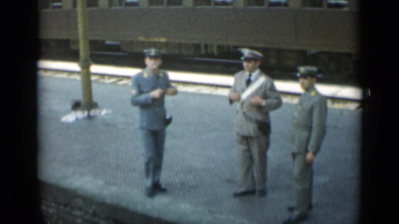 Uniformed men stand on a platform while one appears to hold a cigarette.