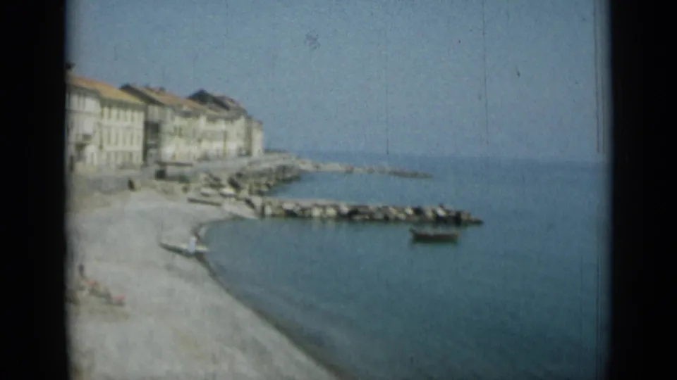 A Monaco waterfront view shows shoreline buildings, a rocky breakwater, calm water, and a small boat in soft 1962 8mm color.