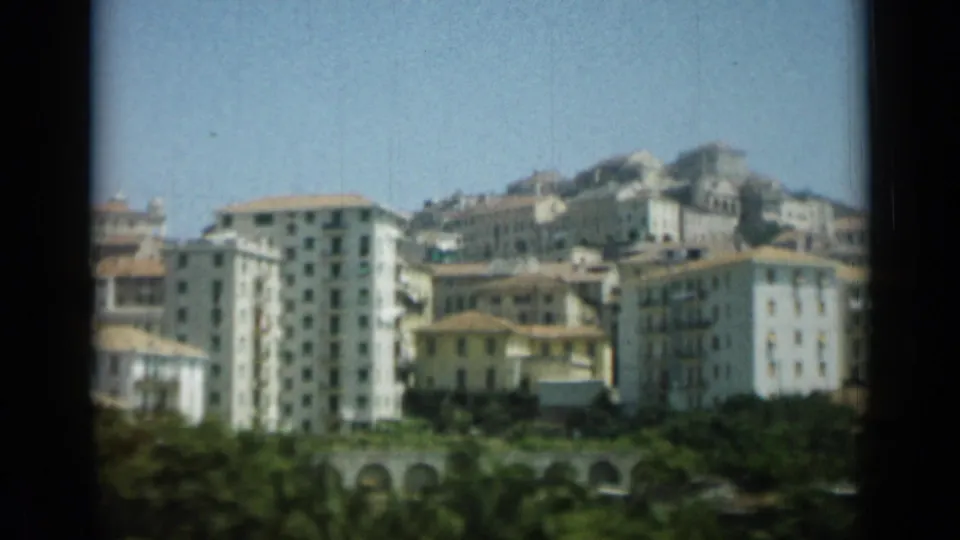1962 Monaco hillside view with apartment blocks, tile roofs, arched structures, trees, and bright blue sky in a home-movie frame.