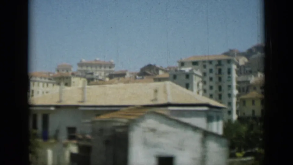 1962 Monaco view across cream waterfront and hillside buildings, framed by dark 8mm gate edges.
