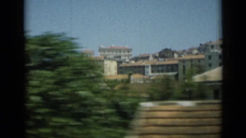 1962 Monaco travel frame with motion-blurred greenery and pale buildings behind it from a passing vehicle.