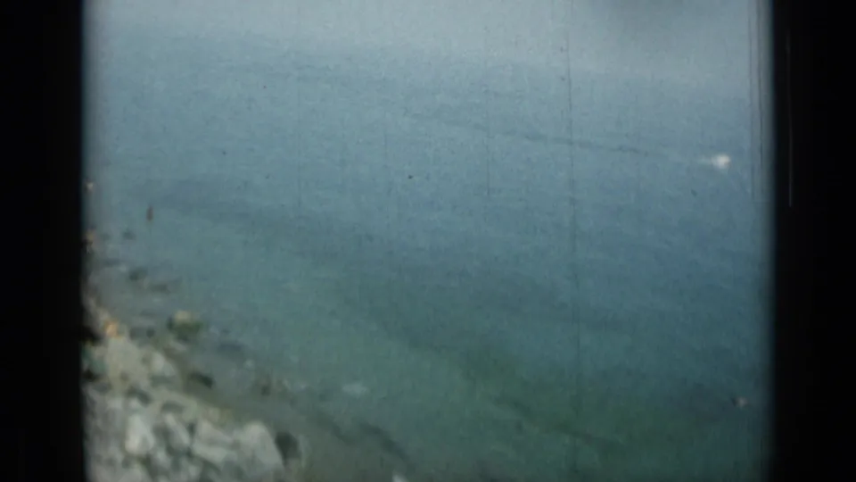 Elevated 8mm view of Monaco or nearby Italian coast, with calm blue-green water and a rocky shoreline below.