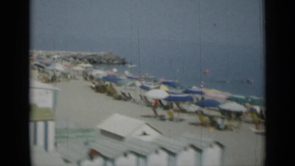1962 Monaco frame showing a soft handheld view of umbrellas and beach huts beside the Mediterranean.