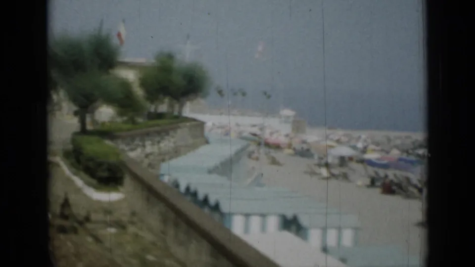 1962 Monaco home-movie view looking past trees and a seawall toward beach huts, boats and the sea.