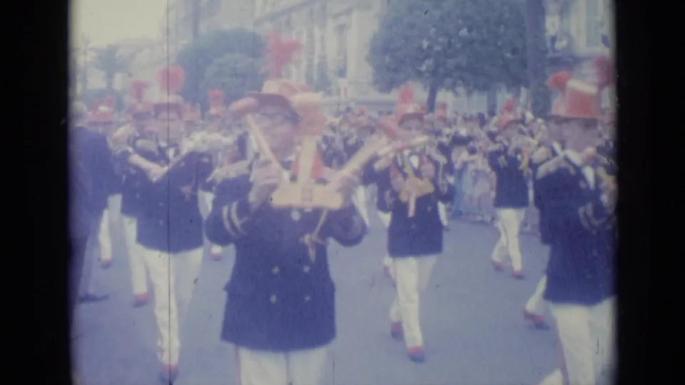 A Nice, France parade scene from 1962 shows brass players in dark uniforms, white trousers, and red plumed hats moving past spectators.