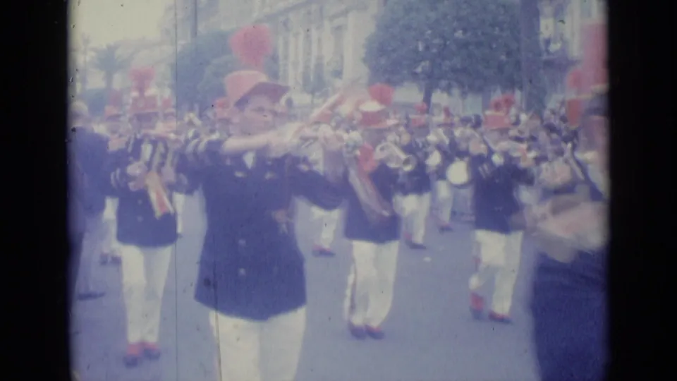 Close spectator-view frame of a trumpet player leading other uniformed musicians in a 1962 Nice street parade.