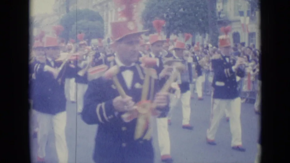 1962 Nice home-movie frame showing uniformed band members in red plumed hats and white trousers marching past spectators.