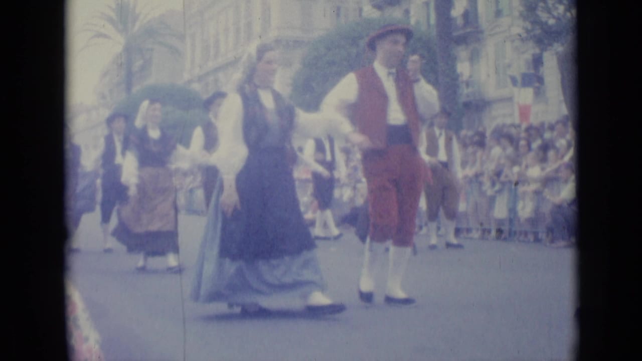 Costumed parade participants walk down a city street as spectators watch from the curb.