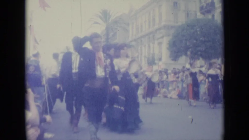 A costumed man appears to wave or lift his hand during the 1962 Nice street parade as spectators line the route.