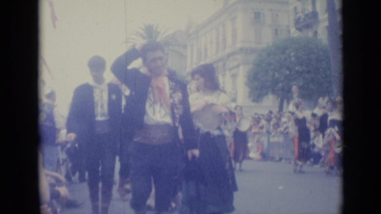 Adults in traditional attire walk along a city street as spectators watch from the sides.