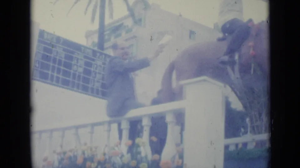 The rider and horse appear beside a white balustrade, blue timing board, and flowers during a 1962 procession in Nice, France.