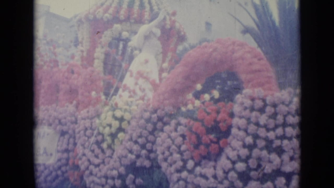 Decorated parade float with a woman standing among flowers and a floral arch.