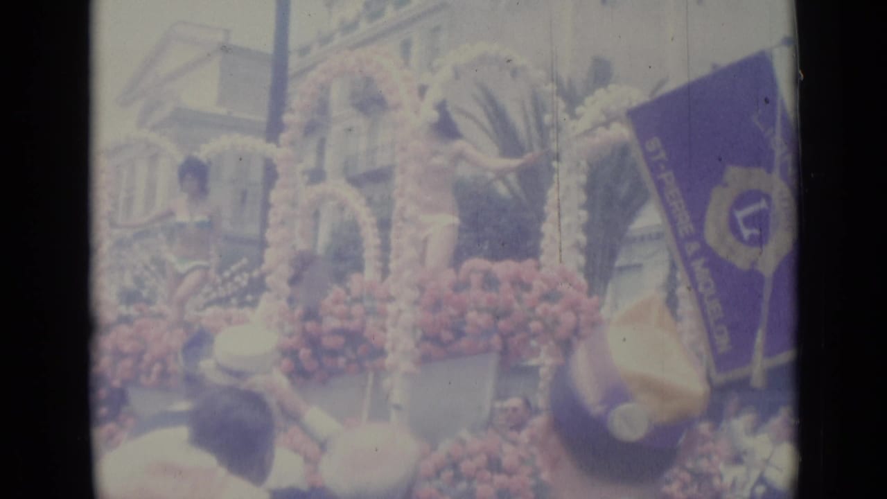 Flower-covered parade float with women in bikinis and a Lions Club flag.