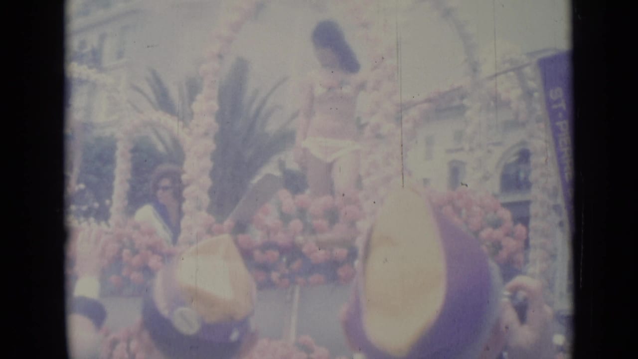 A rider on the Nice parade float appears beside large yellow and purple floral forms as the crowd watches from the street.