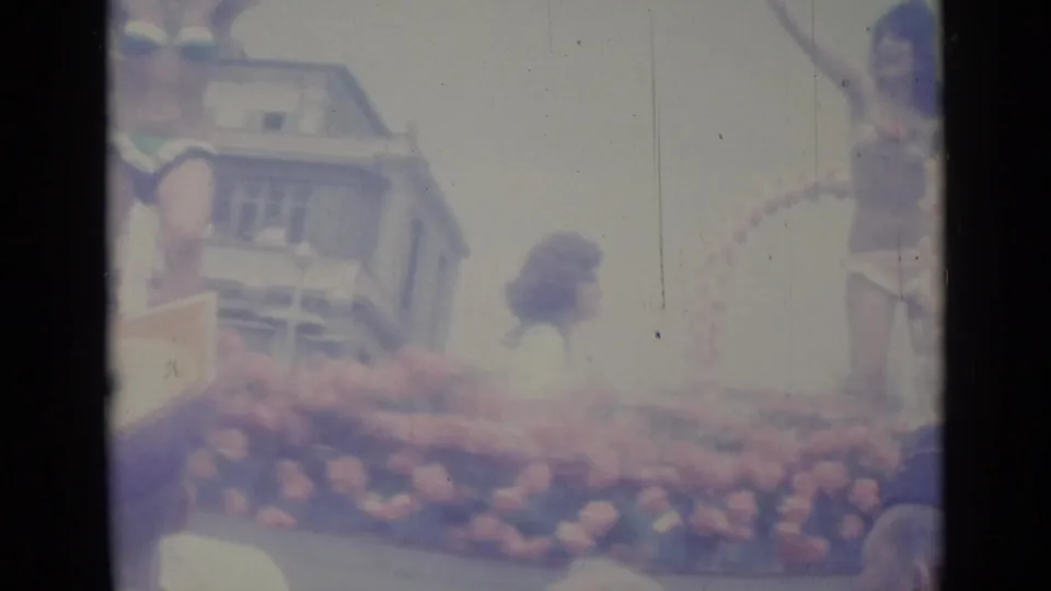 The side of the Nice parade float shows a rider above dense flowers, with street architecture and spectators partly visible.
