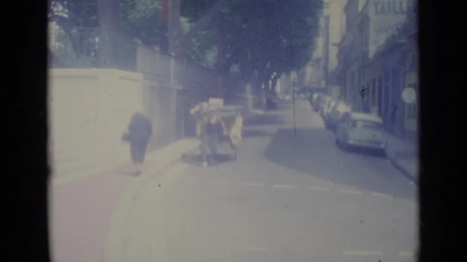 In a 1962 Nice street scene, a loaded cart passes near the center of the road while cars line the curb.