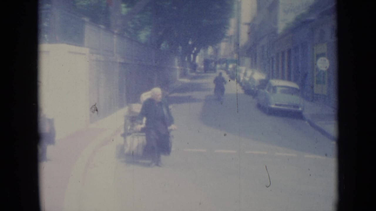 Older woman with a loaded handcart enters the street area as a scooter moves in the distance.